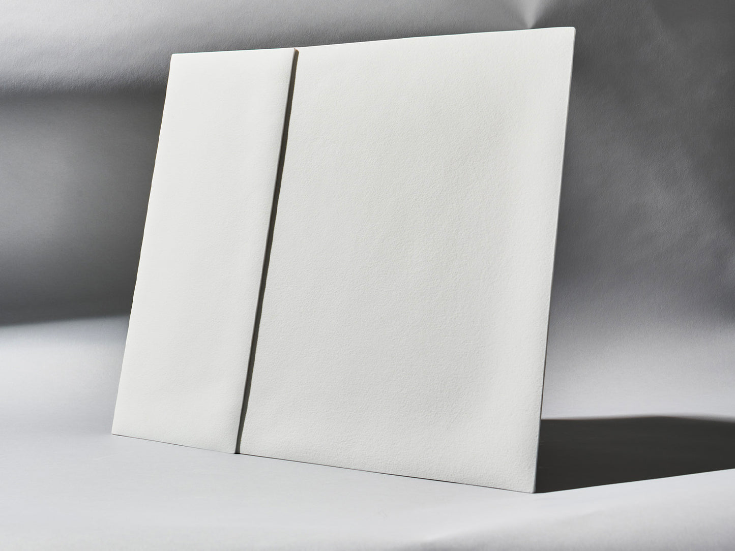 Unglasierte Porzellanfliesen der Serie Lightscape, schräg aufgestellt, mit sanftem Lichtverlauf über der strukturierten Oberfläche.

Unglazed porcelain tiles from the Lightscape series, placed at an angle, with soft lighting across the textured surface.