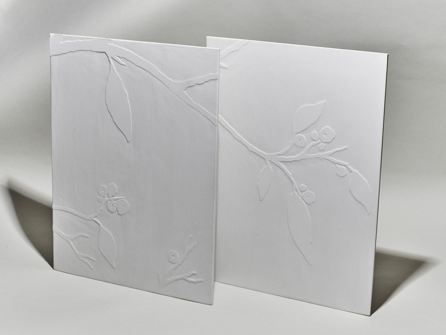 Zwei weiße Porzellanfliesen mit reliefiertem Kirschblütenzweig auf hellem Hintergrund.

Two white porcelain tiles with a relief cherry blossom branch on a light background.