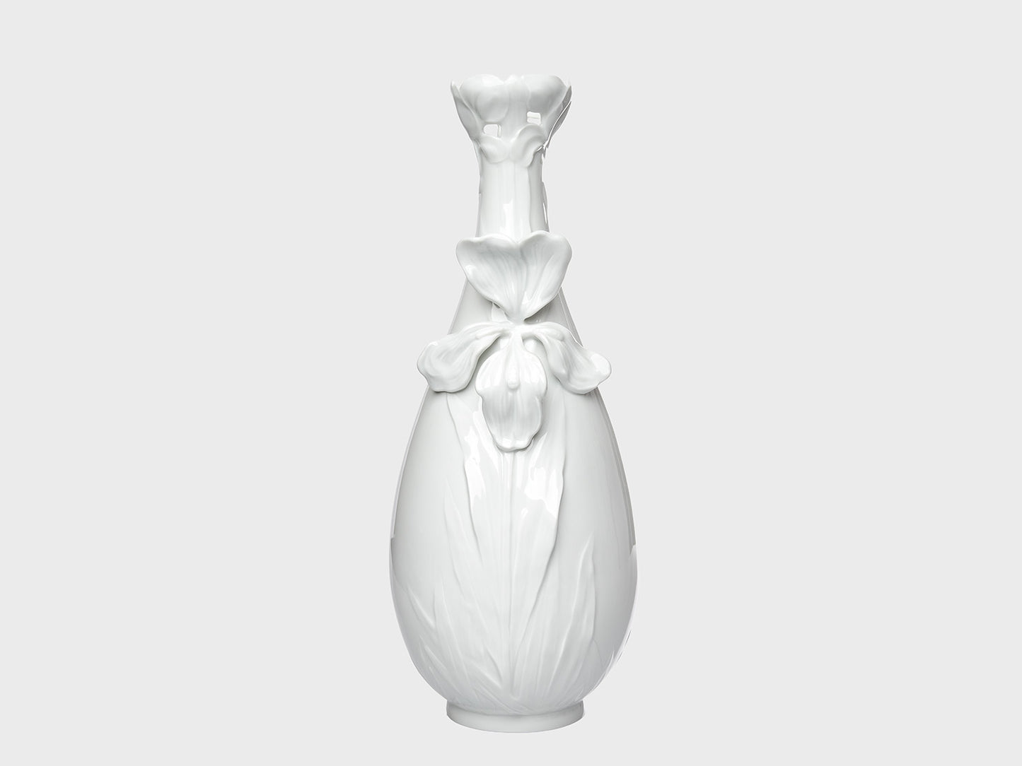 Weiße Porzellanvase mit glänzender Oberfläche und floralen Reliefdetails auf neutral hellgrauem Hintergrund. Die bauchige Form wird durch eine große Blütenapplikation auf der Vorderseite und eine dekorativ geformte, blütenartige Öffnung am Hals ergänzt.

White porcelain vase with a glossy finish and floral relief details on a neutral light gray background. The rounded body features a large flower applique on the front, while the neck is finished with a decorative, blossom-shaped opening.
