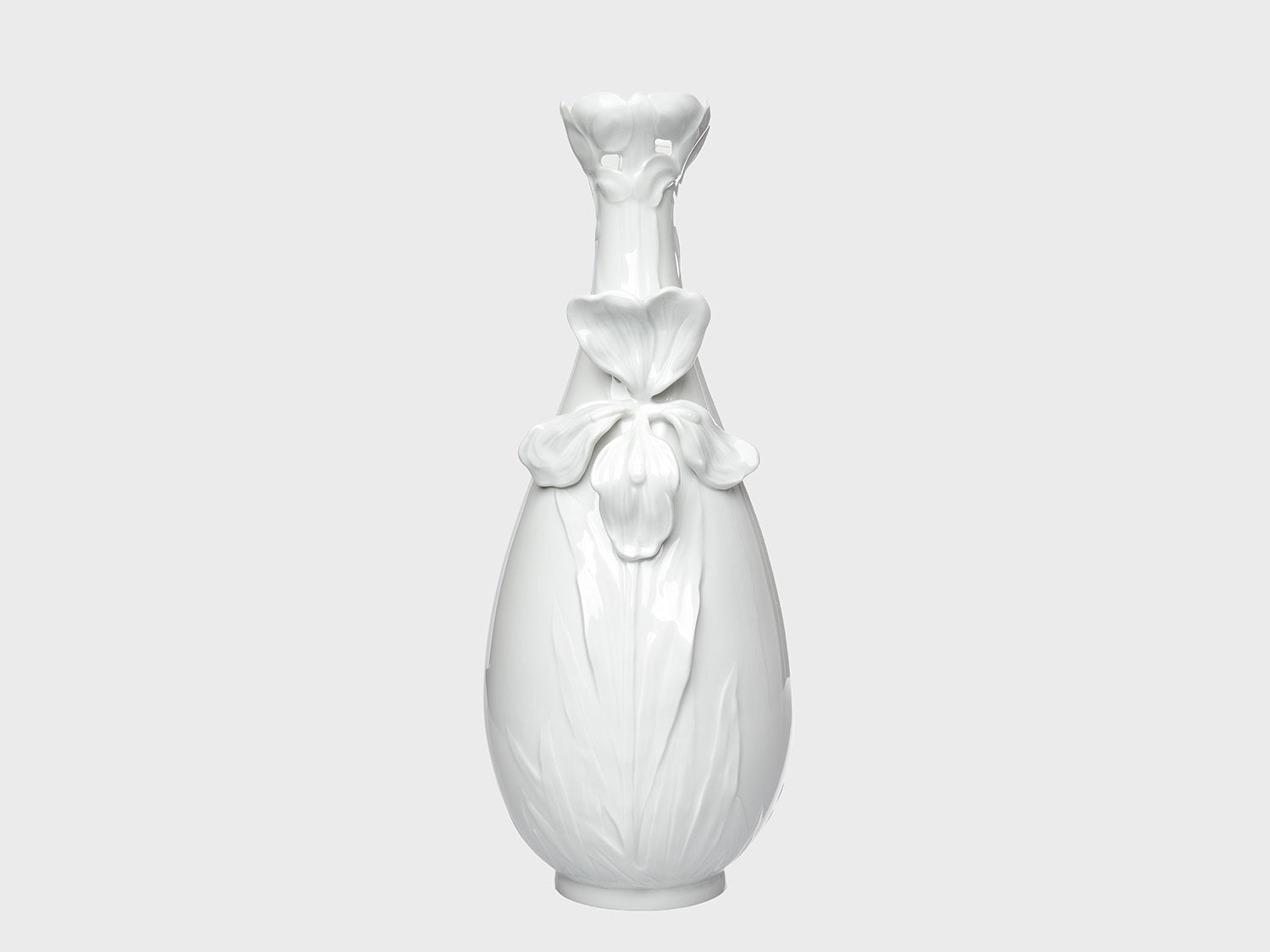 Weiße Porzellanvase mit glänzender Oberfläche und floralen Reliefdetails auf neutral hellgrauem Hintergrund. Die bauchige Form wird durch eine große Blütenapplikation auf der Vorderseite und eine dekorativ geformte, blütenartige Öffnung am Hals ergänzt.

White porcelain vase with a glossy finish and floral relief details on a neutral light gray background. The rounded body features a large flower applique on the front, while the neck is finished with a decorative, blossom-shaped opening.
