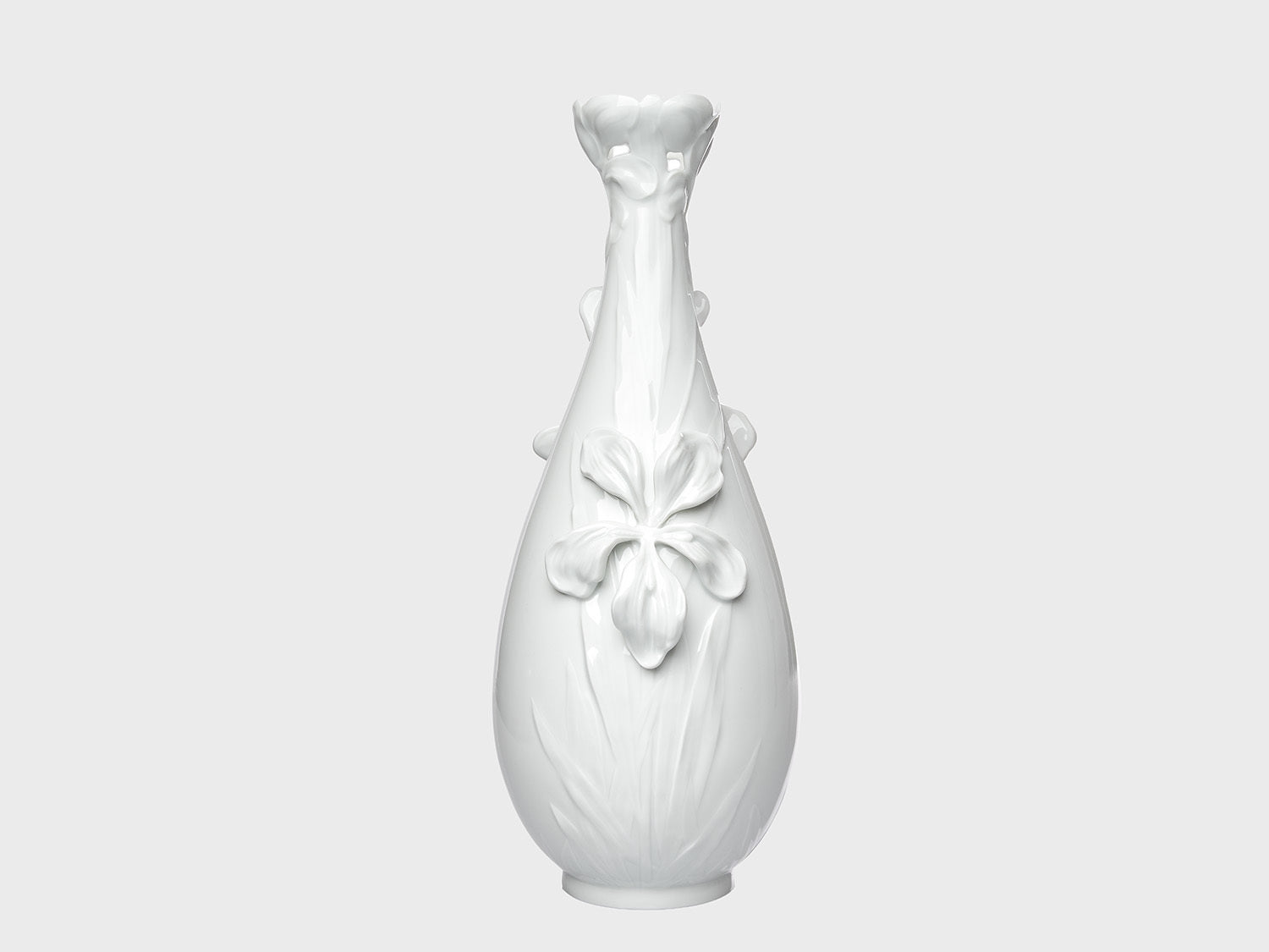 Weiße Porzellanvase mit glänzender Oberfläche und floralen Reliefdetails auf neutral hellgrauem Hintergrund. Die bauchige Form wird durch eine große Blütenapplikation auf der Vorderseite und eine dekorativ geformte, blütenartige Öffnung am Hals ergänzt.

White porcelain vase with a glossy finish and floral relief details on a neutral light gray background. The rounded body features a large flower applique on the front, while the neck is finished with a decorative, blossom-shaped opening.

