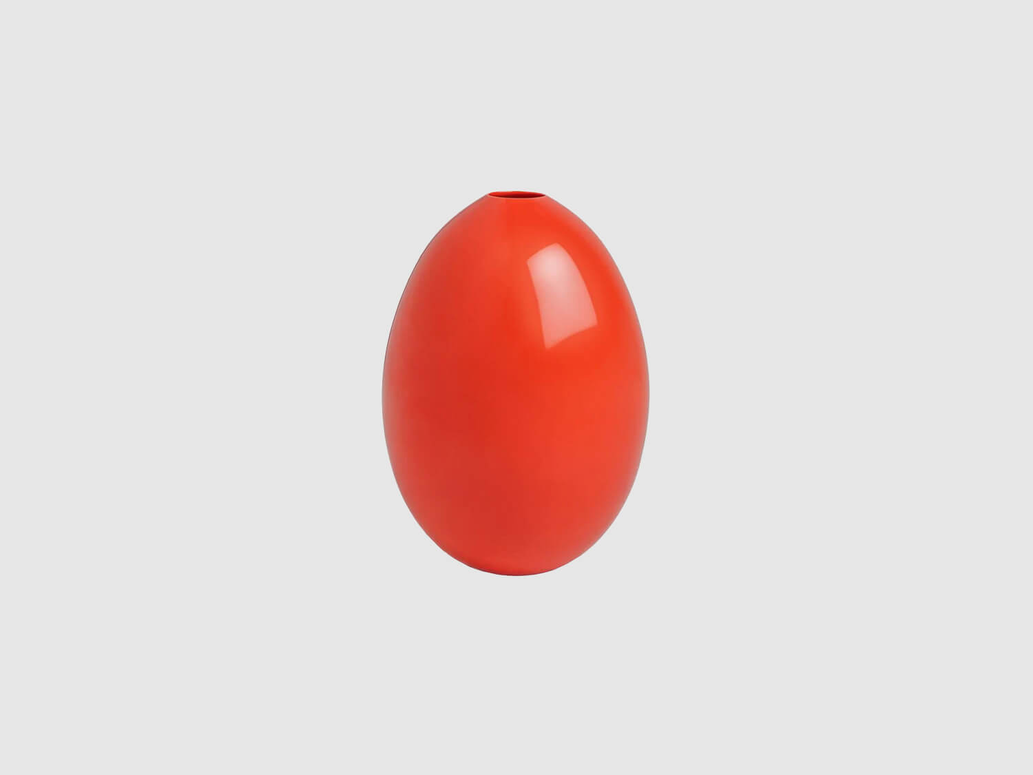 Kleine, eiförmige Vase aus glänzend korallenrotem Porzellan vor hellem Hintergrund.

Small egg-shaped vase in glossy coral red porcelain against a light background.