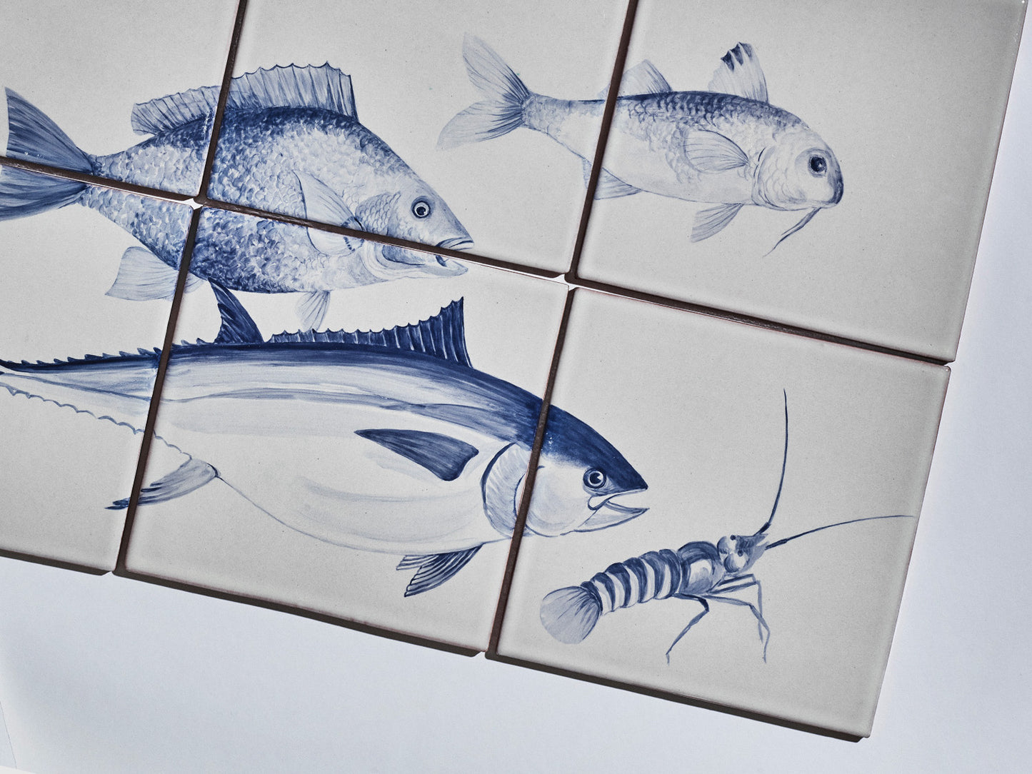Sechsteiliges Fliesenbild mit handgemalten Meeresmotiven in Blau auf hellem Grund: Fische und ein Krebs.

Six-tile mural with hand-painted marine motifs in blue on a light background: fish and a crustacean.