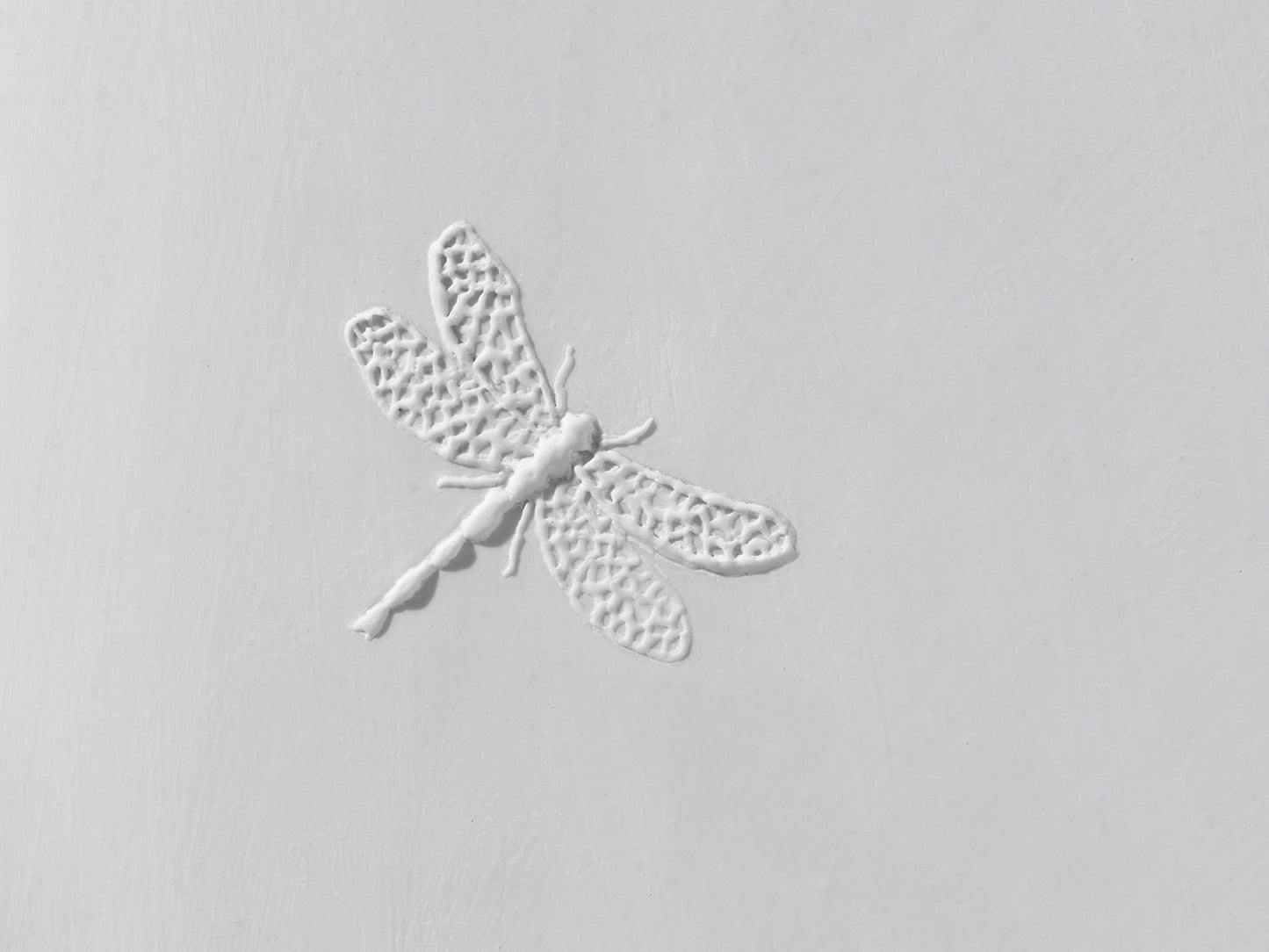 Detailaufnahme des Libellenreliefs auf weißer Biskuitfliese, mit filigraner Flügelstruktur und matter Oberfläche.

Close-up of the dragonfly relief on a white biscuit tile, showing intricate wing structures and a matte surface.