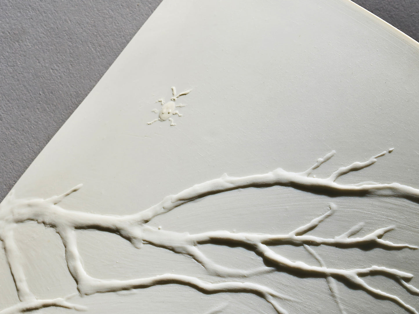 Detailaufnahme des plastischen Zweigreliefs mit Insekt auf weißem Biskuitporzellan.

Close-up of sculpted branch relief with insect on white biscuit porcelain.