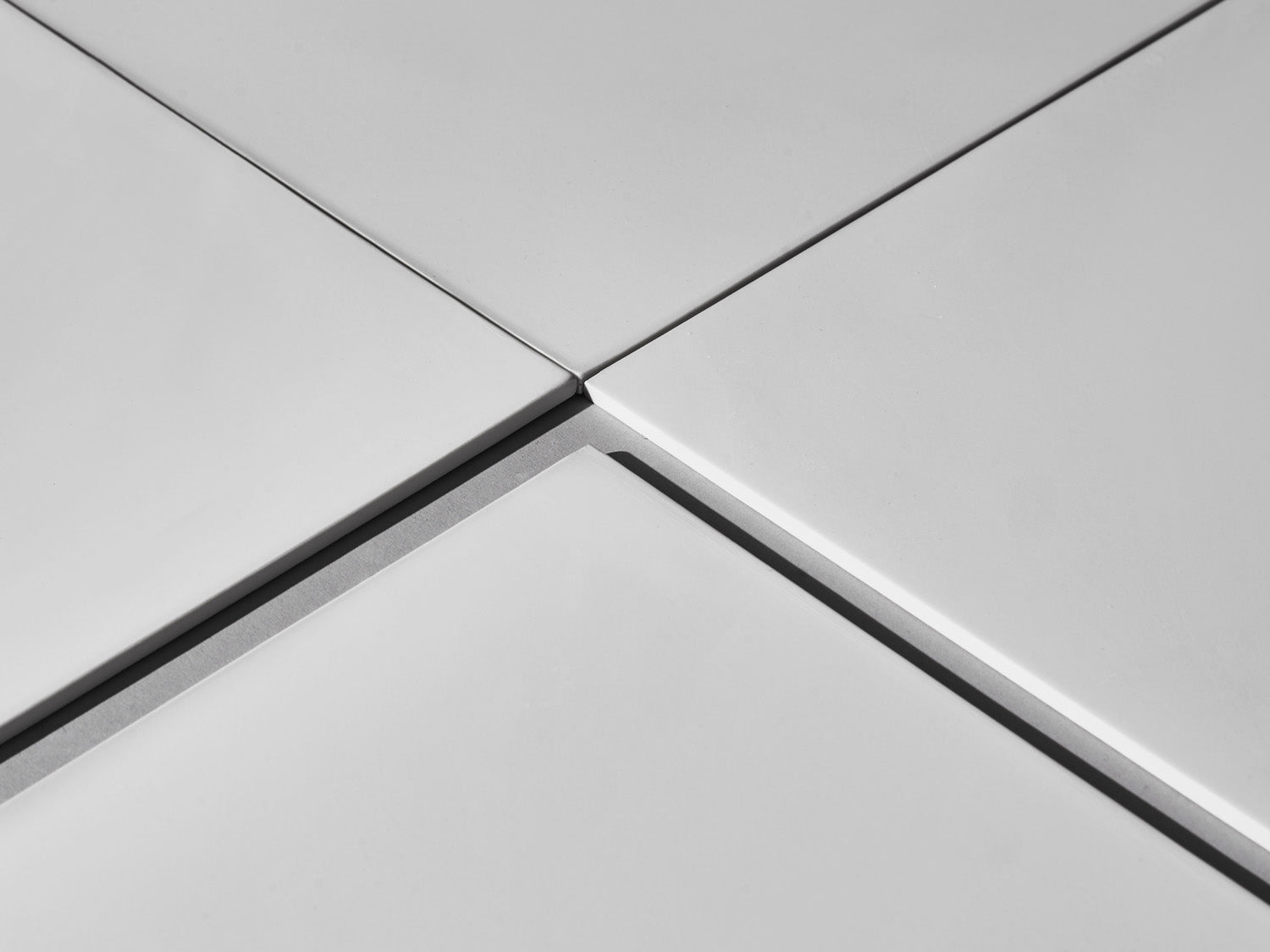 Nahaufnahme der Fugen vier weißer Fliesen.

Close-up of grout line between four white tiles.