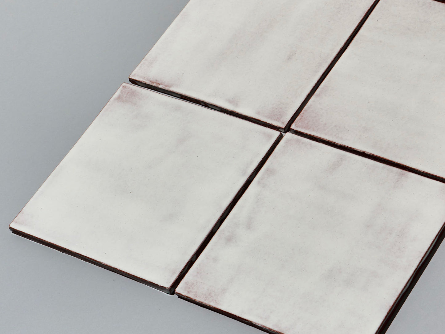 Vier Majolika-Fliesen mit durchschimmernder weißer Glasur in Fugenanordnung.

Four majolica tiles with translucent white glaze arranged with fine grout lines.