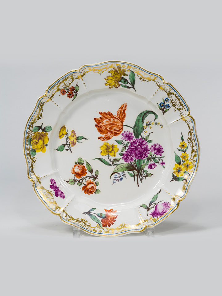 Barocker Porzellanteller mit goldverziertem Rand und bunter Blumenmalerei auf weißem Grund.

Baroque porcelain plate with a gilded rim and colourful floral painting on white background.