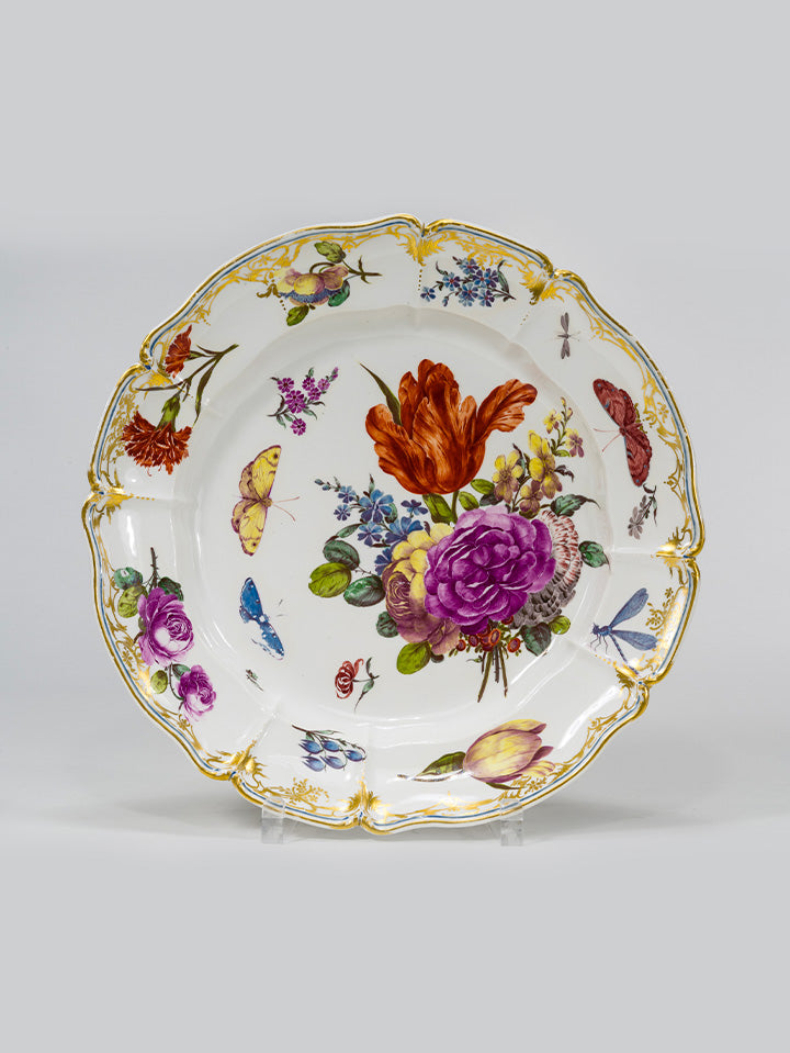 Porzellanteller mit barocker Blumenmalerei und goldverziertem Rand, verziert mit Insektenmotiven.

Porcelain plate with baroque floral painting and gilded rim, decorated with insect motifs.