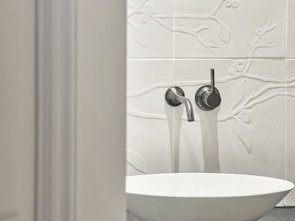 Badezimmerwand mit Kirschblütenrelieffliesen hinter einem modernen Waschbecken.

Bathroom wall with cherry blossom relief tiles behind a modern washbasin.
