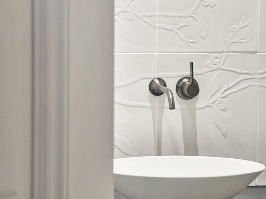 Badezimmerwand mit Kirschblütenrelieffliesen hinter einem modernen Waschbecken.

Bathroom wall with cherry blossom relief tiles behind a modern washbasin.